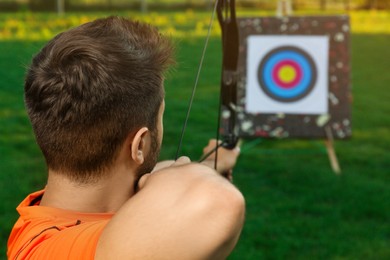 Man with bow and arrow aiming at archery target in park