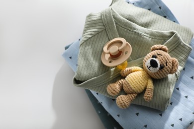 Baby clothes, pacifier and toy bear on light table, top view