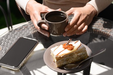 Woman with cup of coffee and tasty dessert at glass table outdoors, closeup