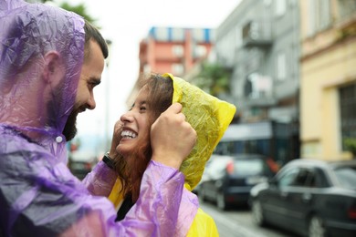 Young couple in raincoats enjoying time together on city street, space for text