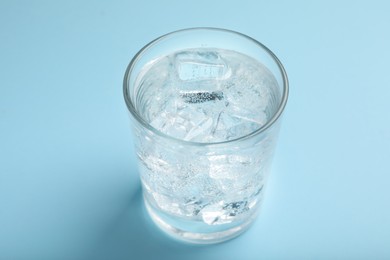 Glass of soda water with ice on light blue background, closeup