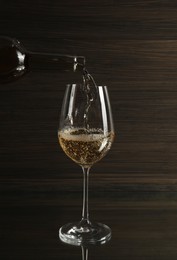 Pouring white wine from bottle into glass on table against wooden background