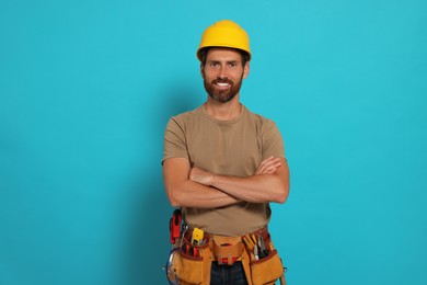 Professional builder in hard hat with tool belt on light blue background