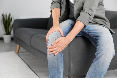 Man suffering from knee pain at home, closeup. Space for text