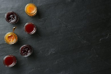 Jars of different jams on black table, flat lay. Space for text