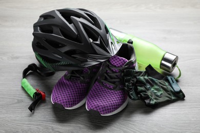 Photo of Stylish bicycle helmet, sneakers, water bottle and fingerless gloves on wooden table