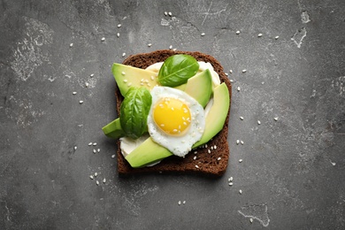 Toast bread with cream cheese, avocado and fried egg on dark background