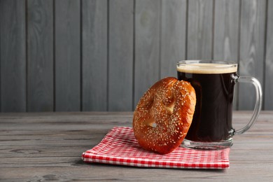 Tasty pretzel and glass of beer on wooden table, space for text