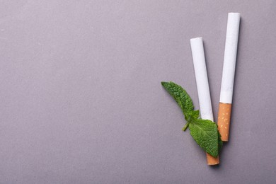 Menthol cigarettes and mint leaves on grey background, flat lay. Space for text