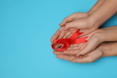 Photo of Woman and girl holding red ribbon on blue background, top view with space for text. AIDS disease awareness