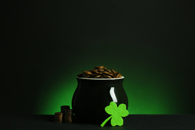 Pot with gold coins and clover on table against dark background. St. Patrick's Day