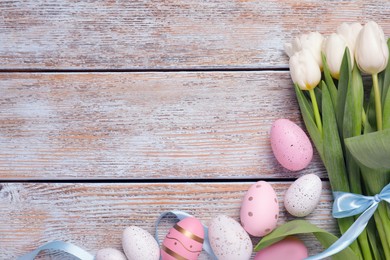 Photo of Many painted Easter eggs, tulip flowers and ribbon on rustic wooden table, flat lay. Space for text