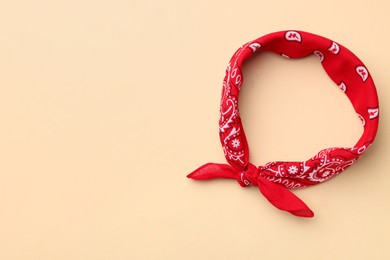 Tied red bandana with paisley pattern on beige background, top view. Space for text