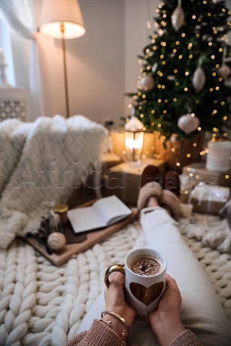 Woman with cup of cocoa in room decorated for Christmas, closeup