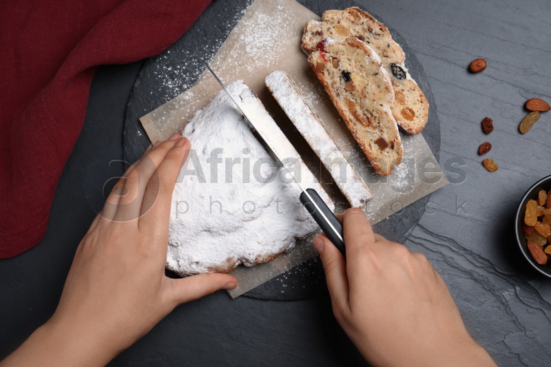 Woman cutting traditional Christmas Stollen at black table, top view