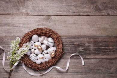 Photo of Many painted Easter eggs, branch of lilac flowers and ribbon on wooden table, flat lay. Space for text