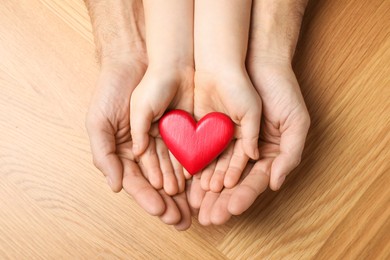 Photo of Man and kid holding red heart in hands at wooden table, top view