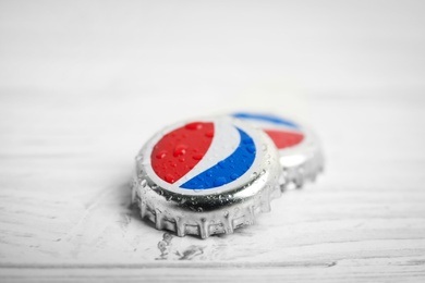 MYKOLAIV, UKRAINE - FEBRUARY 11, 2021: Pepsi lids with water drops on white wooden table, closeup