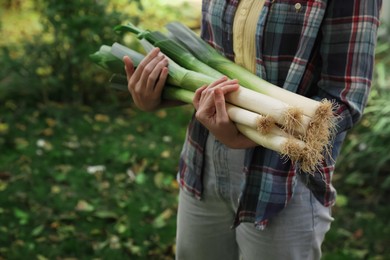 Woman holding fresh raw leeks outdoors, closeup. Space for text