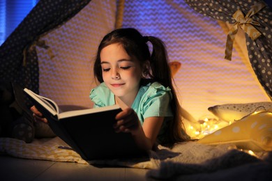 Little girl reading fairy tale in play tent at home