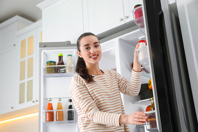 Young woman taking yoghurt out of refrigerator in kitchen, low angle view