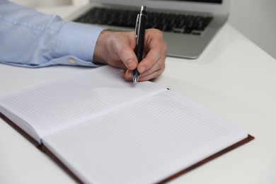 Left-handed man writing in notebook at white table, closeup