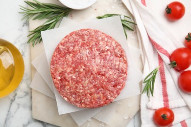 Raw hamburger patties with rosemary, salt and tomatoes on white marble table, flat lay