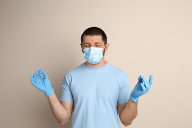 Man in protective mask meditating on beige background. Dealing with stress caused by COVID‑19 pandemic