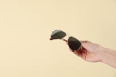 Photo of Woman holding stylish sunglasses on beige background, closeup. Space for text