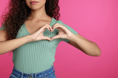 African-American woman making heart with hands on pink background, closeup