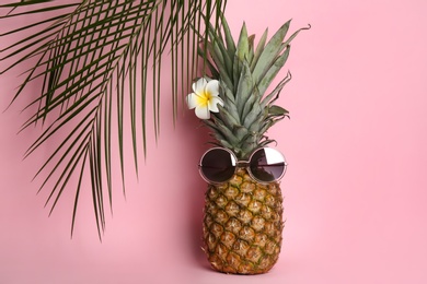 Photo of Pineapple with sunglasses, plumeria flower and palm tree leaves on pink background. Creative concept