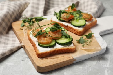 Tasty toasts with cream cheese, shrimps, cucumbers and microgreens served on grey marble table, closeup