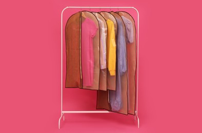 Photo of Garment bags with clothes on rack against pink background