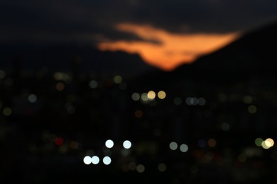 Blurred view of sunset with dark clouds above big mountains and night city