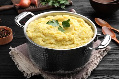 Pot of tasty mashed potatoes with parsley on black wooden table