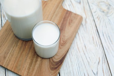 Bottle and glass of tasty fresh milk on white wooden table, closeup. Space for text