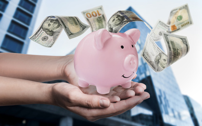 Woman holding piggy bank and American dollars falling outdoors, closeup 