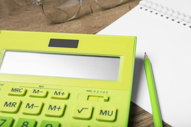 Calculator, notebook, pencil and glasses on wooden table, closeup. Tax accounting