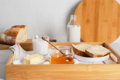 Photo of Jar with honey, milk, butter and bread served for breakfast on table indoors