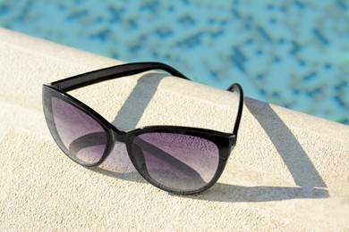Stylish sunglasses near outdoor swimming pool on sunny day, closeup