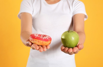 Photo of Concept of choice. Woman holding apple and doughnut on yellow background, closeup