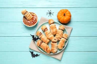 Spooky sausage mummies for Halloween party served on light blue wooden table, flat lay