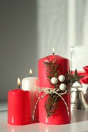 Burning candles with Christmas decor on white table