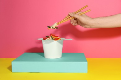Woman eating vegetarian wok noodles with chopsticks from box on color background, closeup