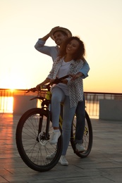 Young couple with bicycle on city waterfront at sunset