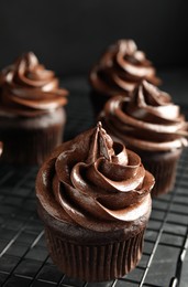 Cooling rack with delicious chocolate cupcakes on black table, closeup