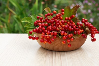 Photo of Bowl with ripe viburnum berries on white wooden table outdoors