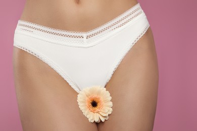 Woman in white panties with gerbera flower on pink background, closeup