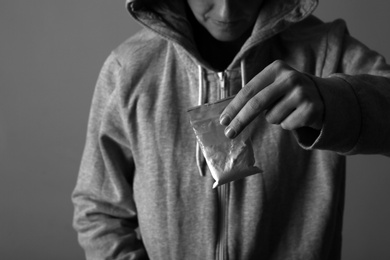 Drug dealer holding bag with cocaine on dark background, closeup. Black and white effect