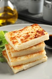 Delicious turnip cake with arugula and soy sauce on plate, closeup